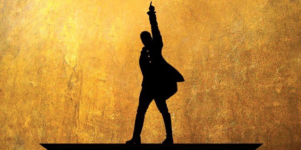 The top part of the poster for Hamilton, the hit musical. It's a siloughette of Alexander Hamilton, legs spread, one arm raised, pointing to the sky. His coat's tails fly. The background is gold.